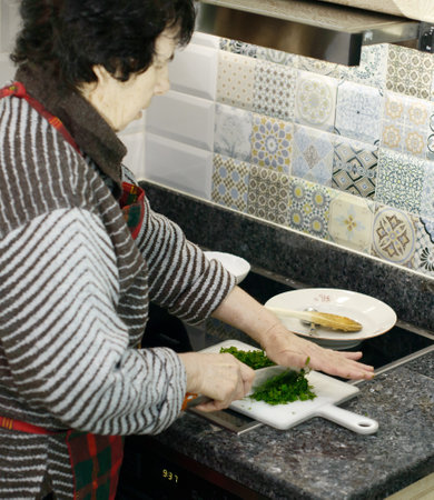 A senior woman is standing at a kitchen counter chopping fresh parsleyの写真素材