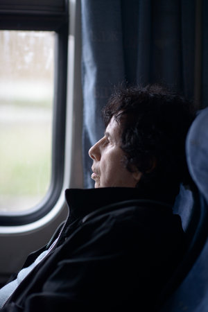 A contemplative elderly woman looks out the window of a moving trainの写真素材