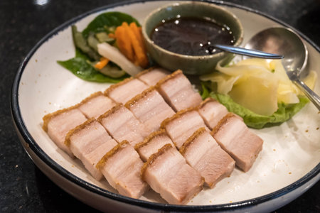 crispy pork belly on a plate with dipping sauce, ginger and pickled vegetables.の写真素材
