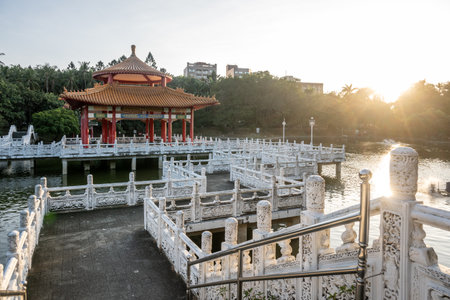 A picturesque view of a traditional Chinese pavilion situated on stilts, with tranquil waters and...