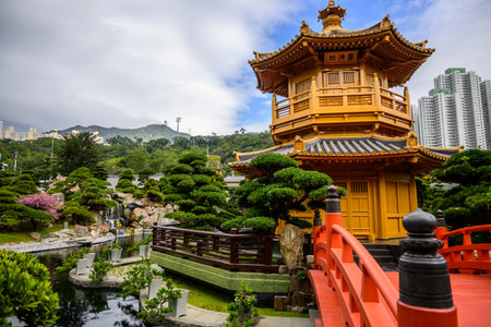 A red wooden bridge with intricately carved railings leads to the golden pagoda, Pavilion of Absolute Perfection, with a black tiled roof at Nan Lian Garden, Hong Kongの写真素材