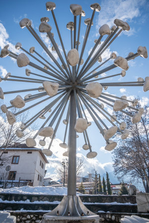 Bansko, Bulgaria - Jan 22, 2025: A low-angle shot of a contemporary starburst, dandelion sculpture made of metal rods and white stones, set against a blue, cloudy winter sky in a public square.のeditorial素材