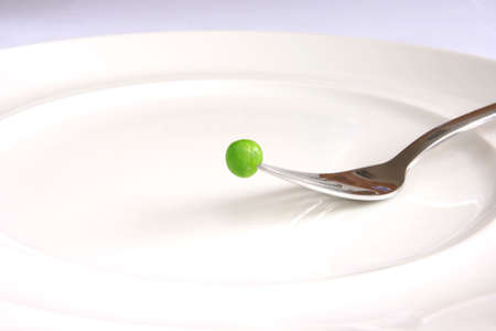 Single fresh green pea above white plate on fork.の写真素材