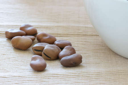 Close up view of scattered dried kidney beans on natural cloth background with part of white bowl