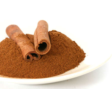 Whole ground cinnamon and sticks on plate white backgroundの写真素材