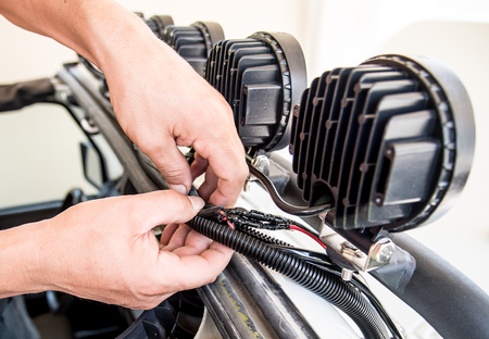 view of the hands of a mechanic inserting electrical wires of roof lights into a protective plastic sheath, upgrading vehiculeのeditorial素材