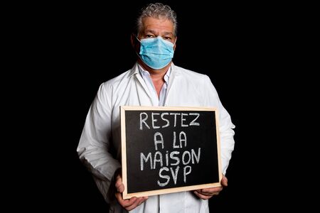 Physician with mask holding a chalkboard on which is written stay home in frenchの写真素材