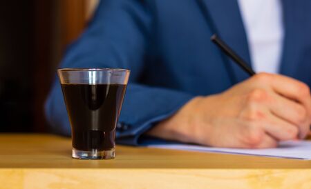 Close-up of a glass of coffee on the table of a well-dressed man in a blue suit and a white shirt...