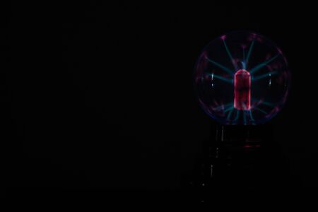 plasma ball or lamp in the dark, with dark black background. Illuminated with pink, red and blue light rays with side space.の写真素材