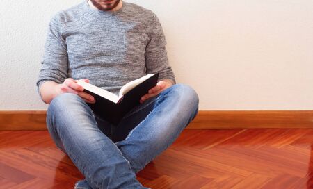 Relaxed young man on the floor at home reading the book.の写真素材