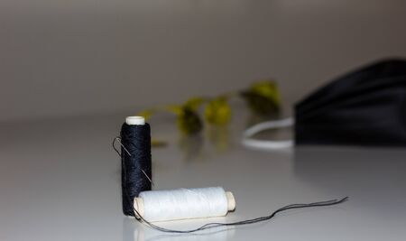 Close-up of spools of black and white thread, a needle, with a mask on blurred background.の写真素材