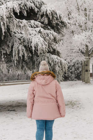 Woman walking in the snow in winter clothes, with red jacket and woolen hat. Girl on snowy path in...