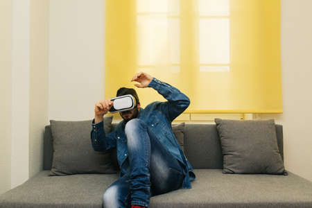 Scared man with glasses and virtual reality headset on the couch at home. innovative concept of 3d...