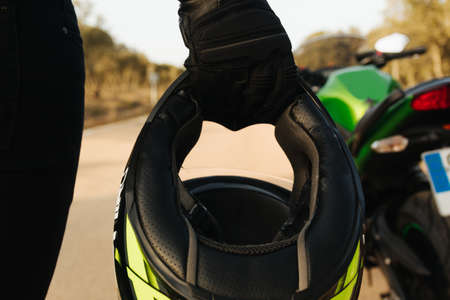 Hand of a biker with a glove holding the protective helmet before getting on his motorcycle on the...