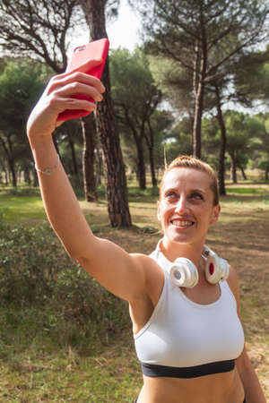 Vertical image of a fitness woman taking a photo or selfie with her smartphone for social media...