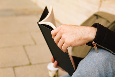 Close-up of the hands of a boy reading a book in the street. Lifestyle, reading and person concept.の写真素材