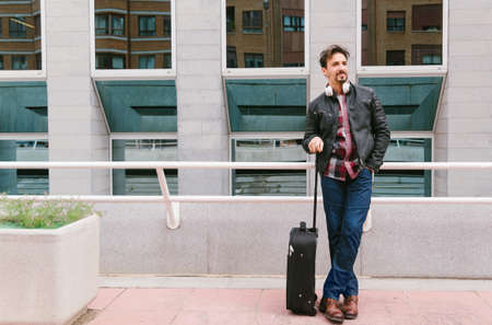 Adult man 30-40 waiting at the station or airport to travel, with suitcase and headphones.の写真素材