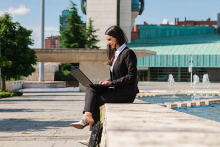 Successful young adult businesswoman working outside the corporate building on a summer day using laptop.の写真素材