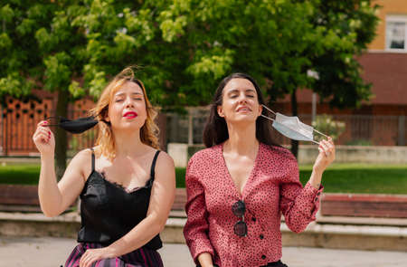 Two women taking off their masks on the street. Concept end of the mandatory outdoor mask. End of...