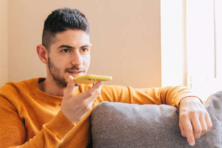 Mid adult man in yellow clothes on gray background from home, sending a voice message from his smart...