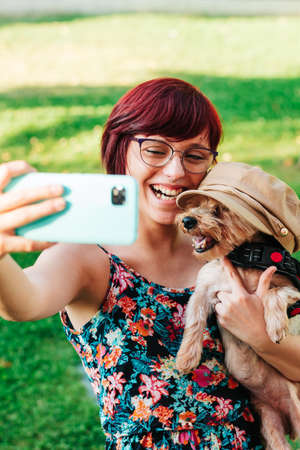 Vertical image of a happy and funny young woman taking a selfie photo with her yorkshire dog...