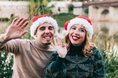 Happy young adult couple waving at camera on video call via laptop on Christmas day. Wallpaper for video call.の写真素材