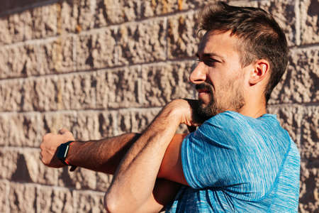 Caucasian man in his 30s stretching and warming up the muscles of the arm, forearm, triceps and shoulder, before and after outdoor training. sport, workout and health concept.の写真素材