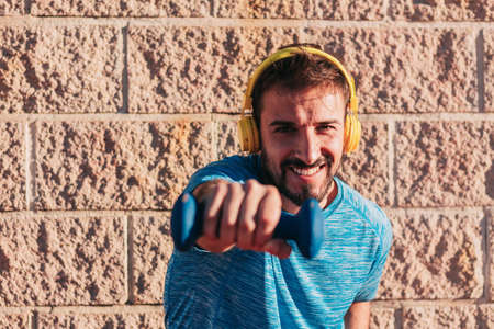 Male athlete lifting and holding a light weight or dumbbell, enjoying and having fun during a workout. With yellow headphones. Empty copy space and concept of sports equipment and healthy life.の写真素材