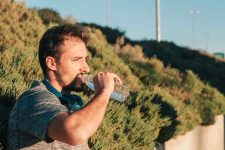 Caucasian person drinking water from a bottle in nature. Concept of hydration, health care, sport and healthy lifestyle.の写真素材