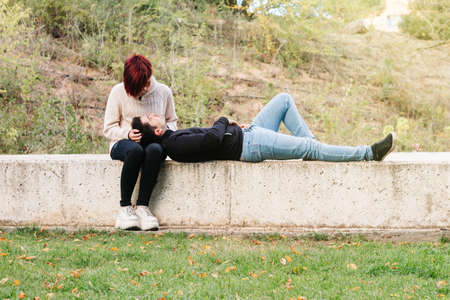 Young man lying relaxed on a wall in the park, with his head on his partner, while she strokes his hair.の写真素材