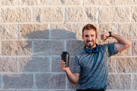Male athlete, young adult, 30 years Caucasian, with a shaker of sports supplements of protein, creatine, bcaa. Looking at camera, smiling, showing his muscles and empty copy space.の写真素材
