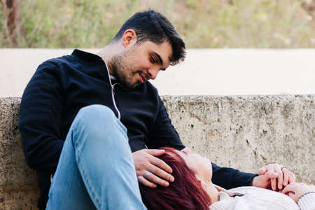 Relaxed young couple sitting in the city park, talking in a tender and loving way.の写真素材