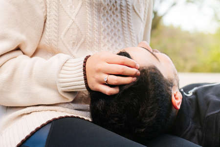 Close-up of a woman's hand with a gold and diamond engagement ring, caressing her partner's head...