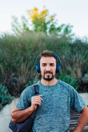 Vertical image Young man dressed in sportswear and bag, walking down the street with his blue headphones listening to music and looking at the cameraの写真素材