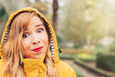 Close-up portrait of a smiling pretty woman wearing yellow raincoat outdoors, with an expression of surprise, doubt and complicity at the drop in temperatures and the weather forecast. Copy space on the right.の写真素材