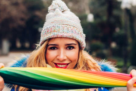 Young adult woman smiling and happy, in winter, showing a very colorful umbrella to the camera.の写真素材