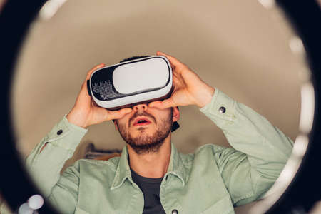 Young adult male influencer, trying out virtual reality and metaverse goggles, while recording an...