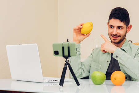 Young adult male recording with a smart phone his healthy eating vlog. Sitting at the table with...