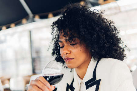 Woman sommelier tasting a glass of red wine in a wine cellar. Elegant woman in her 30's smelling and enjoying a glass of wine in a restaurant.の写真素材