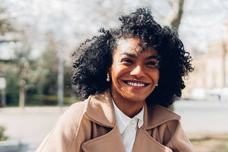 Front view of a happy woman in coat with curly hair in park looking away. Brazilian woman with a face of fun and happiness.の写真素材