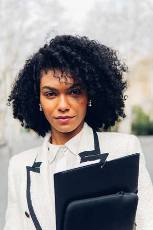 Vertical image of a serious businesswoman posing with folders looking at camera outdoors.の写真素材