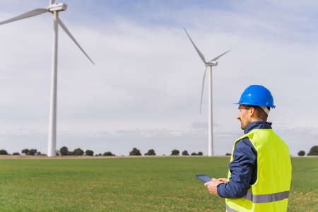 Engineer in a wind energy field using his digital tablet. Man with individual protection equipment...