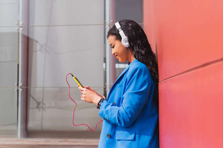 Young woman in her 20s using her smart phone with copy space. African student in modern clothes using social media with her mobile phone.の写真素材