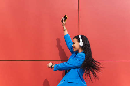 Girl dancing nonchalantly in the air in an urban scene. Woman on a red background, happy and crazy, dressed in retro 90s style blue clothes.の写真素材