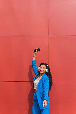 Relaxed young american woman on red background listening to music with satisfied face. Concept of music, playlist, relax, fun, dance, urban.の写真素材