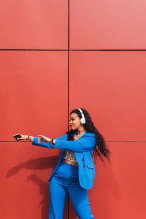 Dance student, training outdoors, wearing modern stylish blue clothes, with a red wall in the background. Concept of joy, street art, youth and vitality.の写真素材