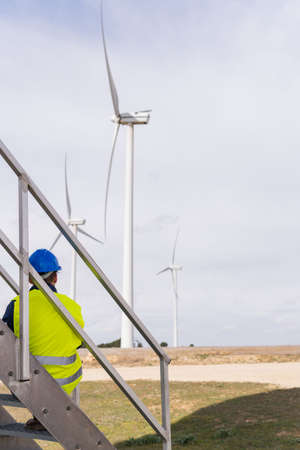 Vertical shot of an unrecognizable worker looking at the wind power park. Concept of engineering, renewable energy, green, clean energy, future, energy self-sufficiency and climate change.の写真素材
