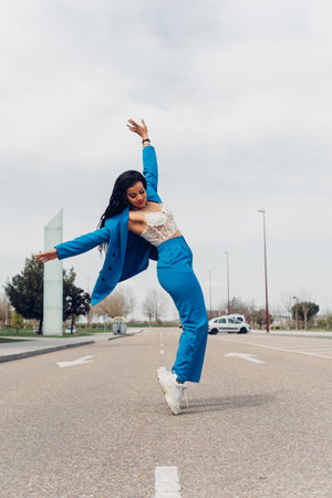 Young adult woman dancing break dance in the street. African teenager in stylish trendy blue outfit Dancing urban dance outdoors.の写真素材
