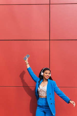 Funny and cheerful black woman dressed in blue, Dancing while listening to music. Fashion portrait of hipster african girl with funny curly hairstyle, modern urban style of 90s. Vertical copy-space.の写真素材