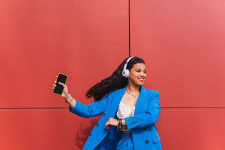Young black woman in her 20s with curly hair, wearing a 90s, 80s retro style blue outfit, dancing hip hop against a red wall, dynamic and fun expression.の写真素材